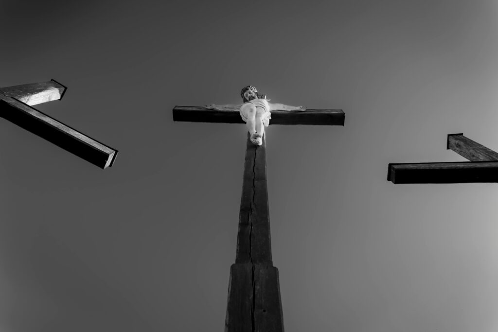 Dramatic black and white photograph depicting three crosses with a central crucifixion scene against a clear sky.