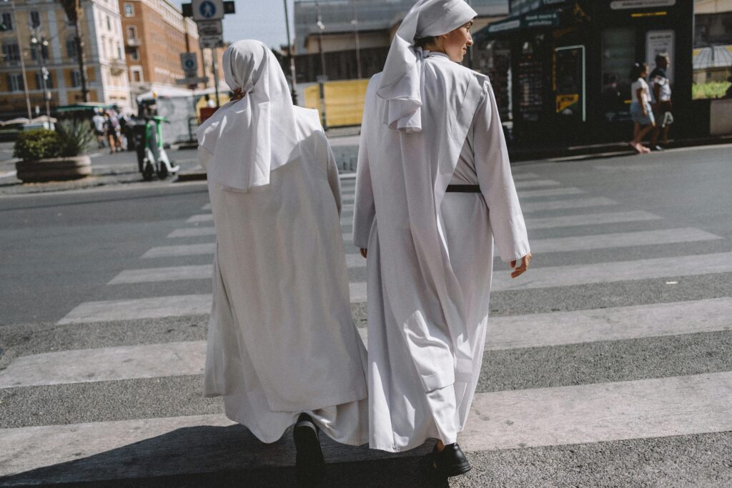Two nuns in white habits cross a street in Vatican City, showcasing urban spirituality.