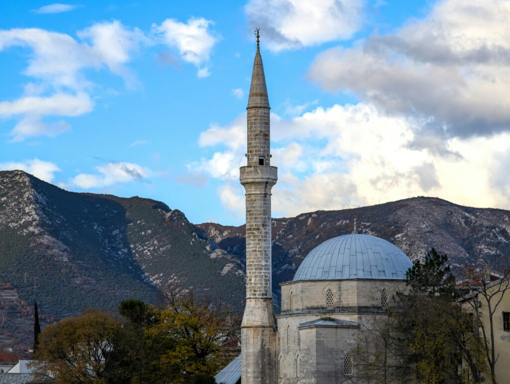 Historic mosque with a tall minaret set against a mountainous backdrop under a bright sky.