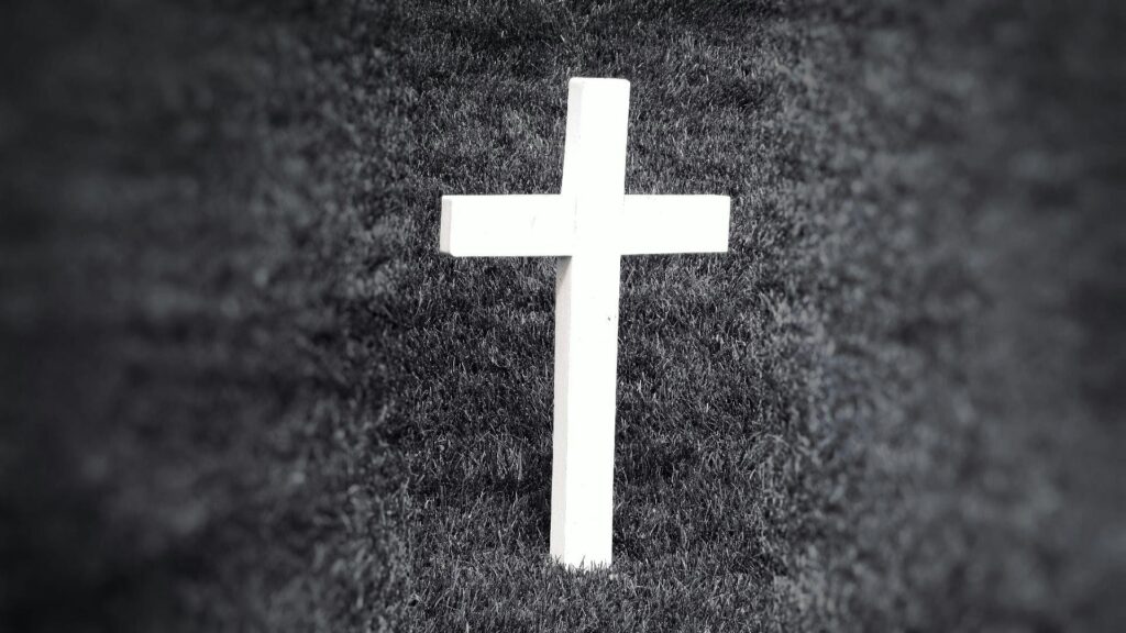 Black and white image of a cross standing in grass, symbolizing spirituality and remembrance.