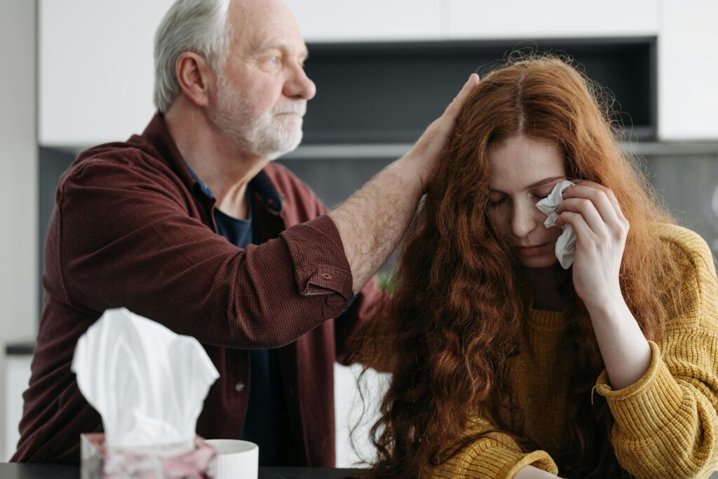 A father consoles his distressed daughter indoors, showcasing love and support.