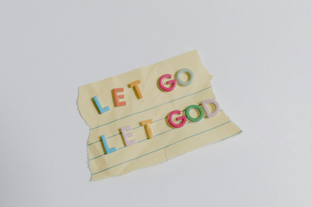 Colorful letters spell 'Let Go, Let God' on torn yellow lined paper.