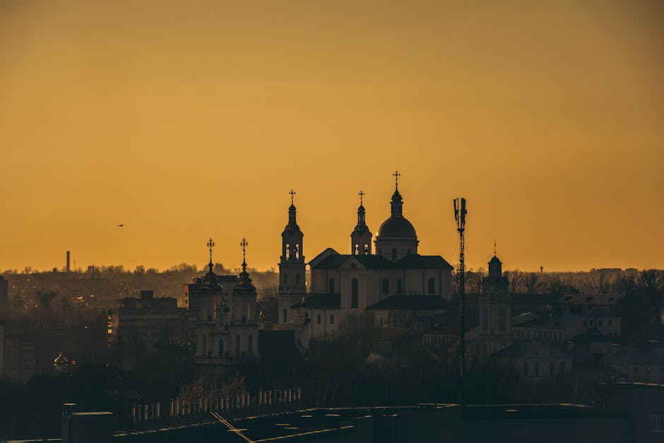 Silhouette of a cathedral with towers and dome under an orange sunset sky.